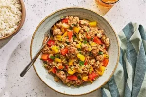 Cooked ground turkey with red and yellow bell peppers and fresh herbs in a rustic bowl