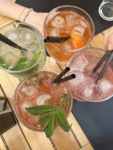 An overhead view of four different colorful iced probiotic drinks with fresh mint and straws on a wooden table, symbolizing a variety of healthy choices for gut health.