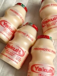 Small plastic bottles of Yakult probiotic fermented milk drink with red foil lids on a light background.