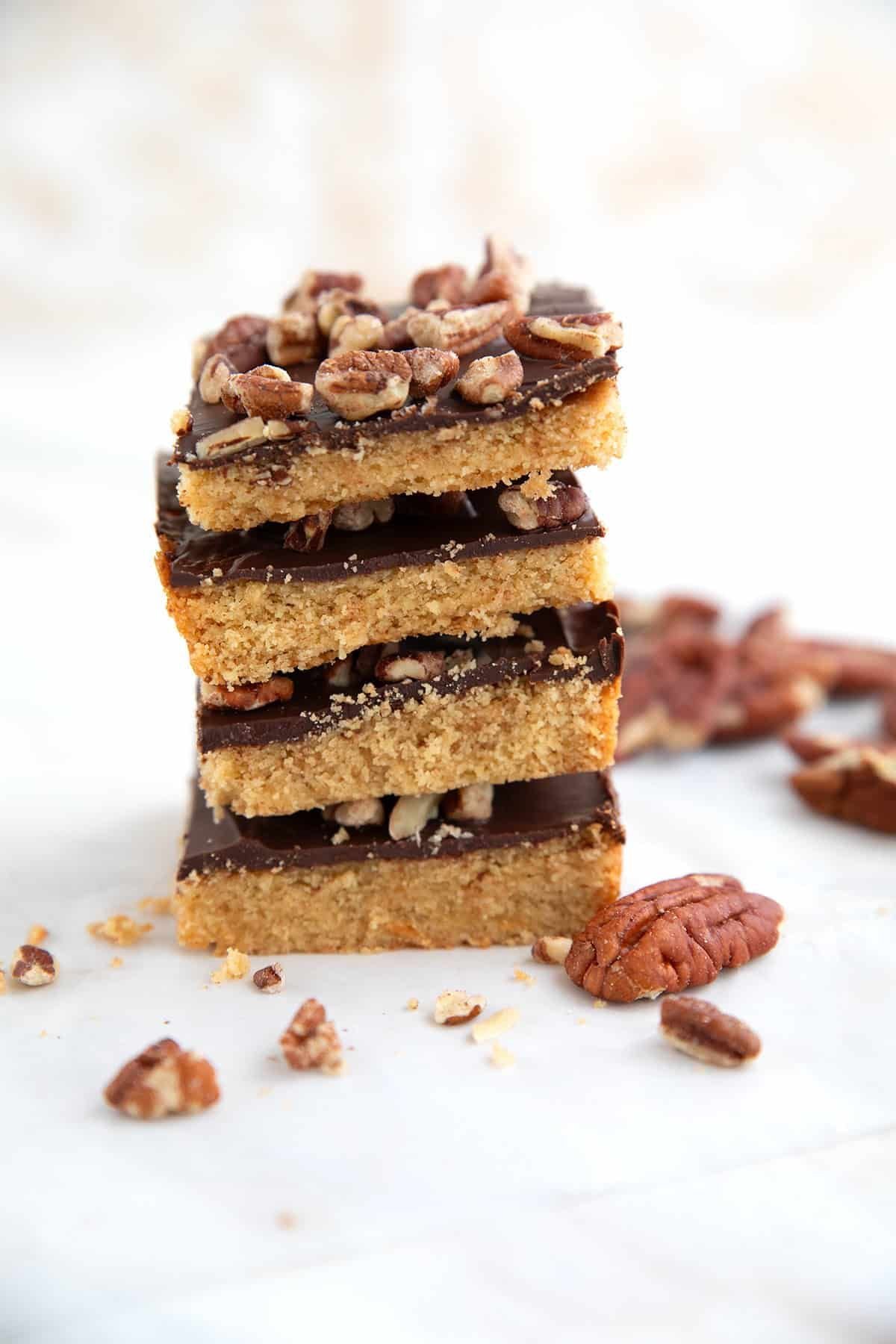 A tall stack of homemade Low Carb Desserts featuring shortbread-style bars topped with dark chocolate fudge and chopped pecans on a light surface.