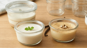 Three clear glass cups on a wooden table, one holding layered vanilla panna cotta, one single panna cotta, and one baked egg custard, all illustrating easy prep-ahead no-carb diet dessert recipes.